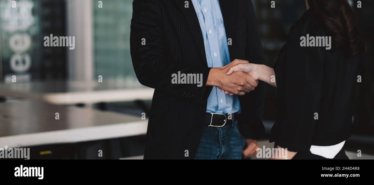 Glückliche, positive Geschäftspartner, die das Treffen abschließen. Geschäftsmann und -Frau stehen im Büro, schütteln die Hände, lächeln, reden. Handshake-Konzept Stockfoto