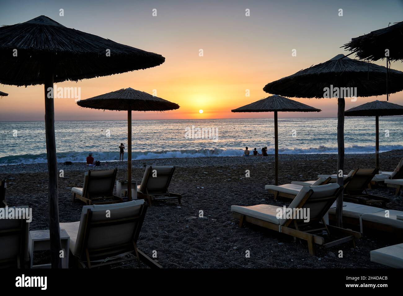 Foto von Sonnenschirmen und Liegestühlen am Strand in Coral Bay, Zypern bei Sonnenuntergang Stockfoto