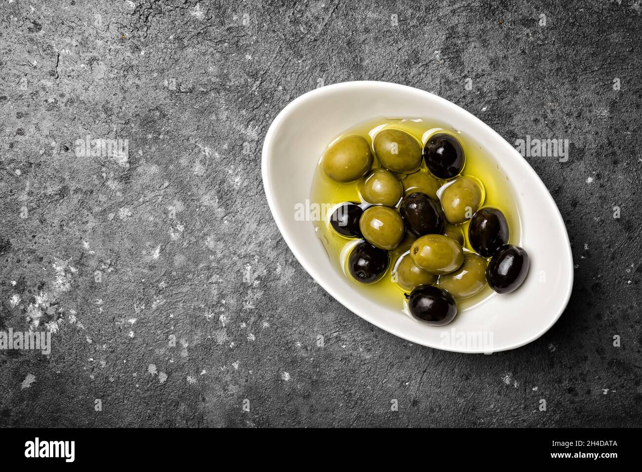 Draufsicht auf geschmackvolle Mischung aus grünen und schwarzen Oliven auf grauem Beton-Hintergrund mit Kopierfläche Stockfoto