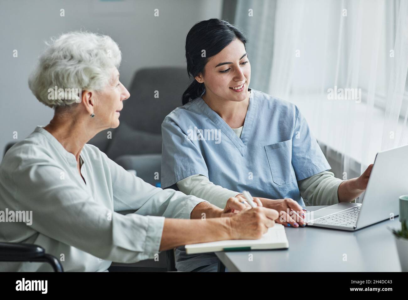 Porträt einer lächelnden weiblichen Betreuerin, die älteren Frauen hilft, die zu Hause einen Laptop benutzen und Platz kopieren Stockfoto