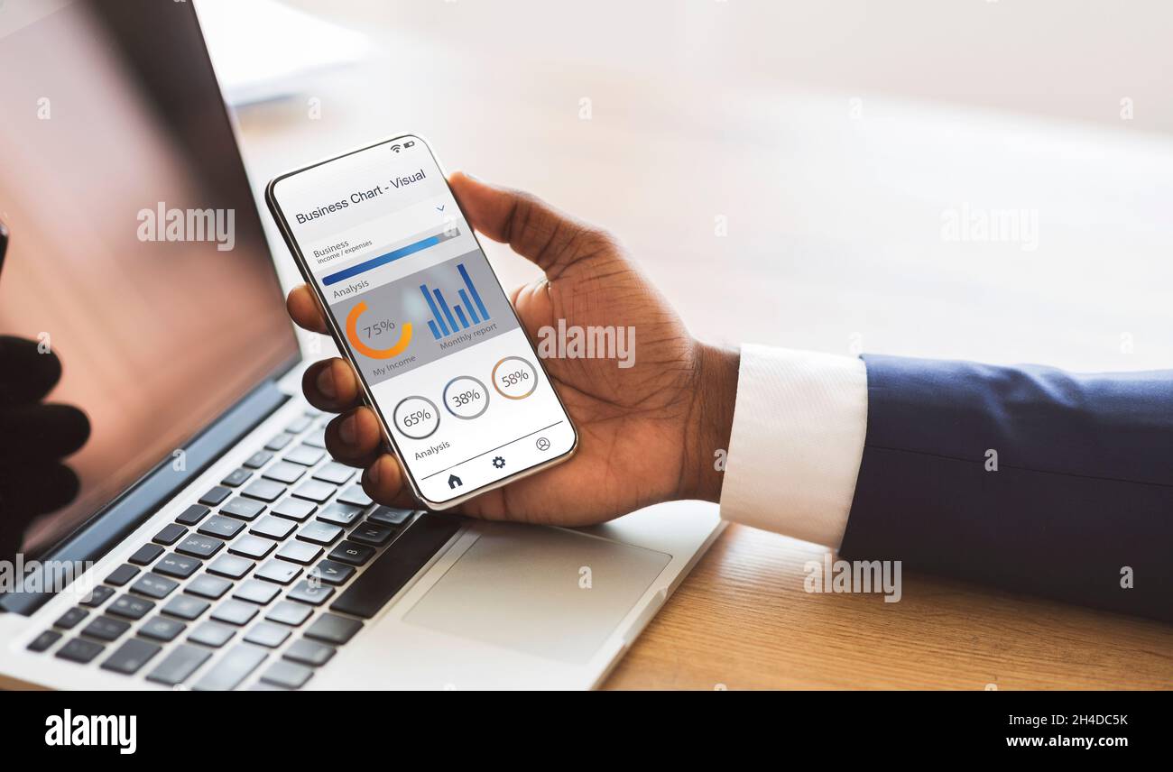 Millennial african american Geschäftsmann mit Laptop, nutzt Smartphone mit Finanz-Business-Chat-App auf dem Bildschirm Stockfoto