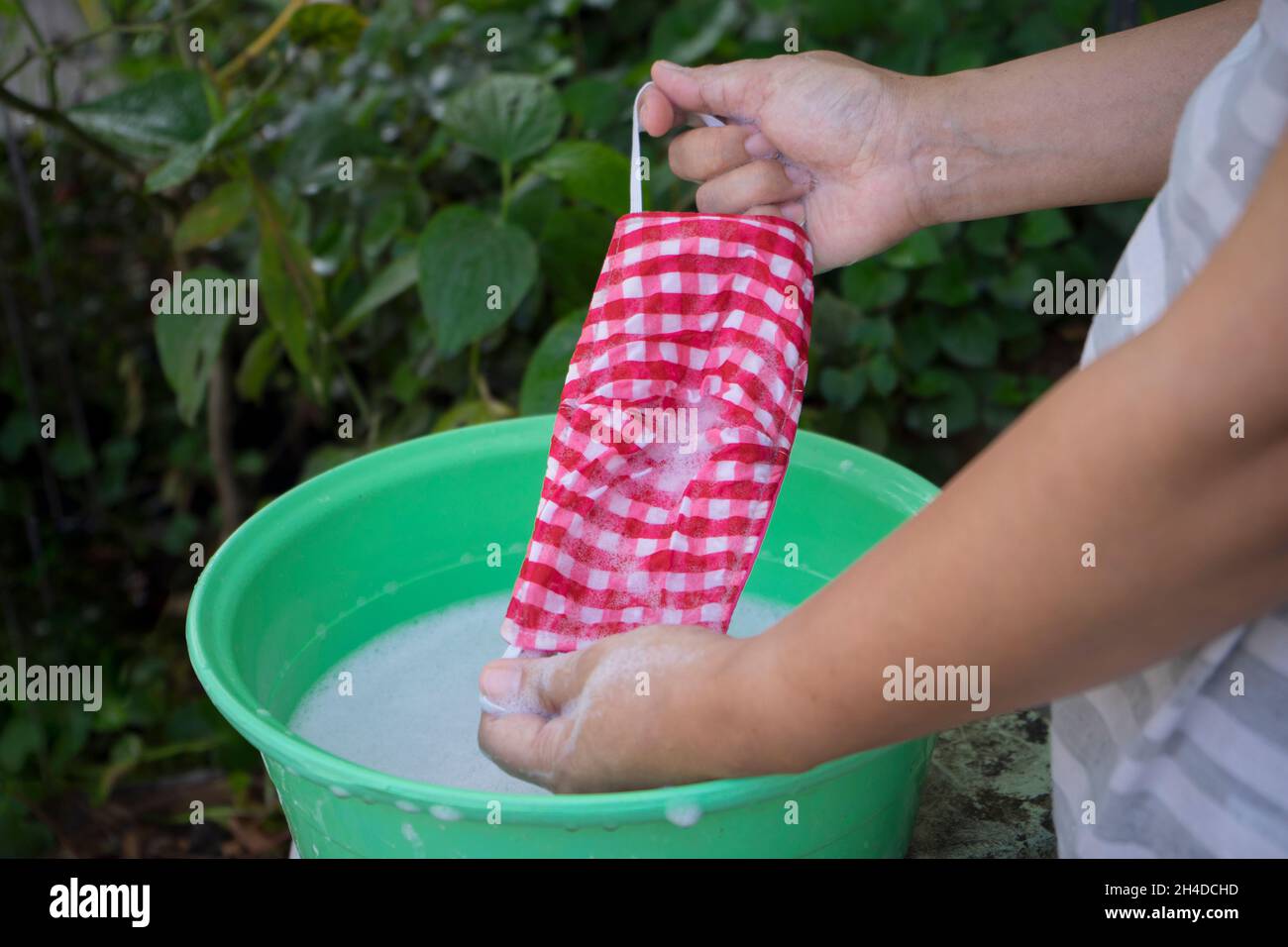 Frau Hand Waschen einer Maske mit in Wasser gelöstem Reinigungsmittel. Das Waschen der Masken desinfiziert und spart Geld, um wieder verwendet zu werden. Stockfoto