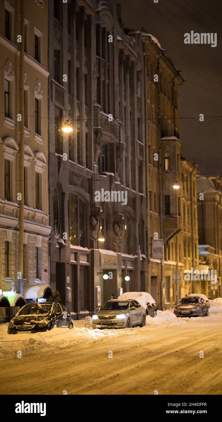 Winterstadt bei Nacht: Leere Stadtstraße mit Auto unter Schnee nach Schneefall und leuchtenden Straßenlaternen Stockfoto