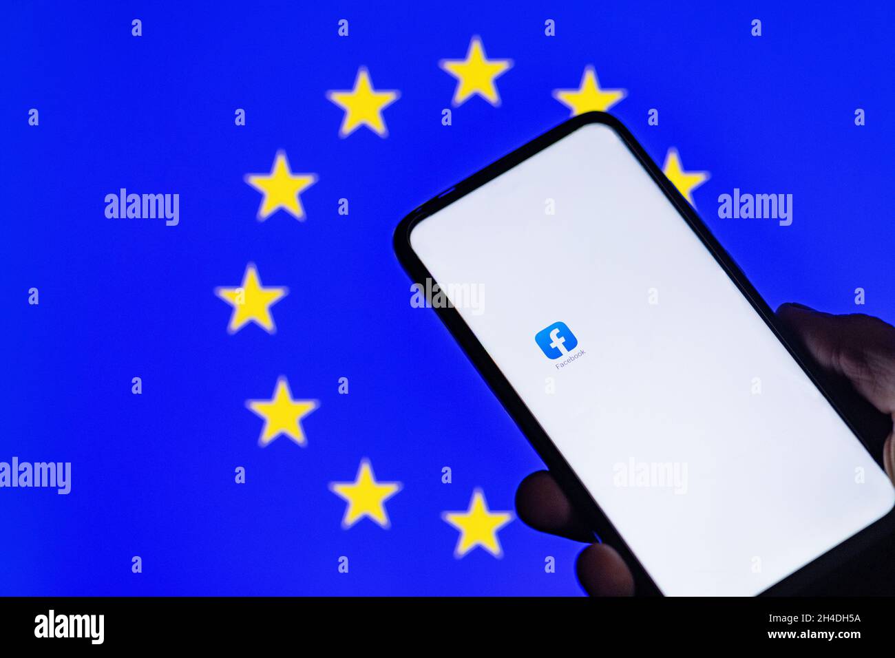 Vilnius Litauen 01 NOV 2021 Silhouette von Mann Hand hält Smartphone mit Facebook-App auf weißem Bildschirm in verschwommener EU-Flagge Backgro angezeigt Stockfoto