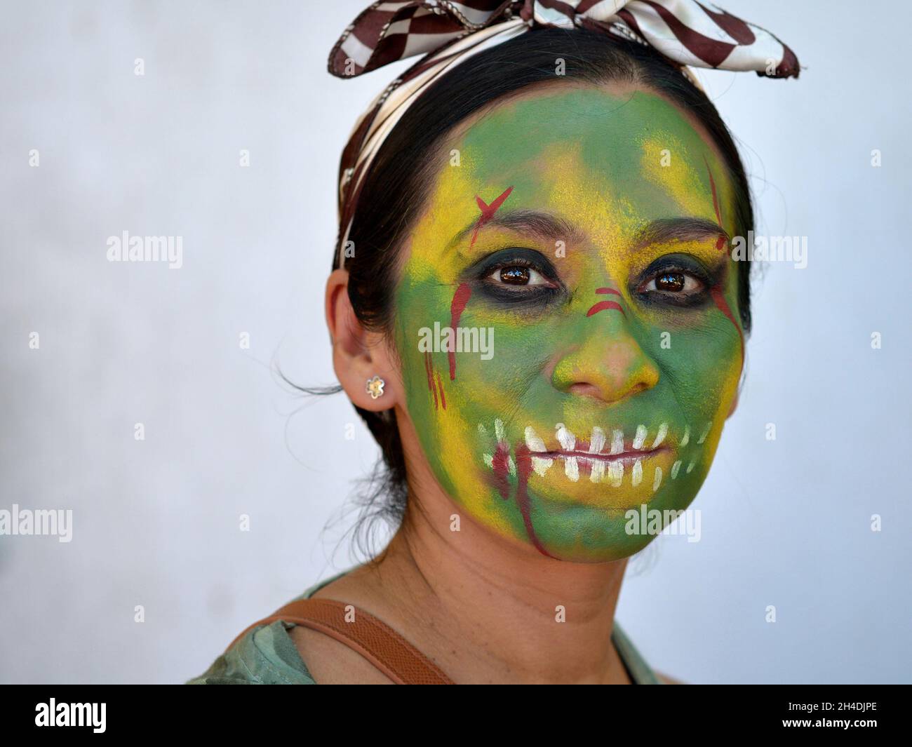 Die junge mexikanische Yucatecan-Frau mit grün gemaltem Zombie-Gesicht schaut den Zuschauer für den Tag der Toten (Dia de los Muertos) an. Stockfoto