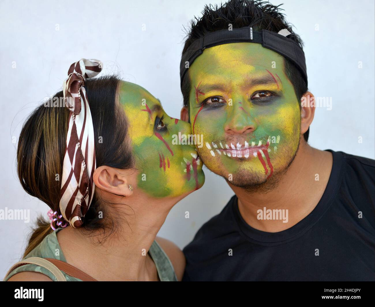 Küssende junge mexikanische Yucatecan Paar mit grün gemalten Zombie-Gesichter für den Tag der Toten (Dia de los Muertos) posiert für die Kamera. Stockfoto