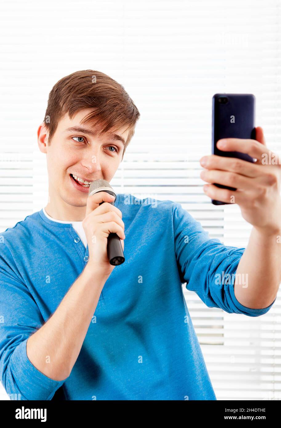 Junger Mann mit Mikrofon singt ein Lied und schaut am Telefon Stockfoto