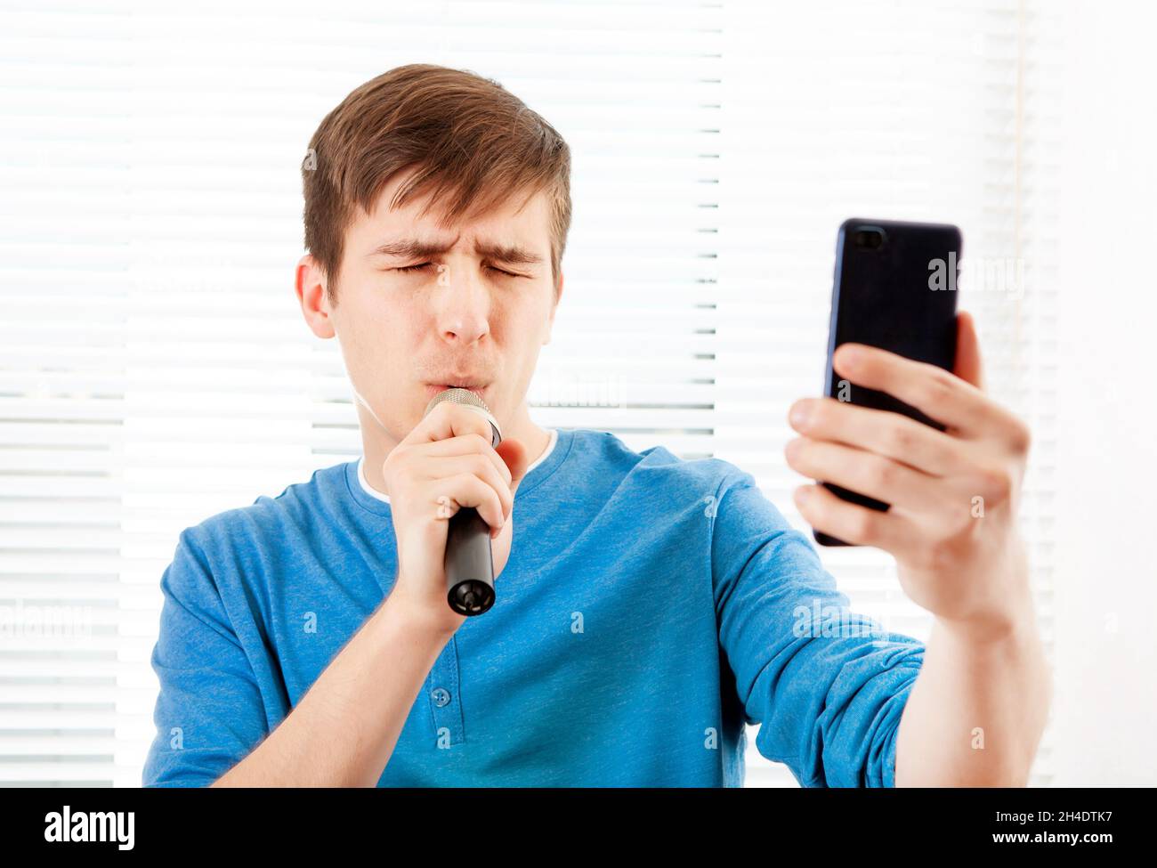 Junger Mann mit Mikrofon singt ein Lied und schaut am Telefon Stockfoto