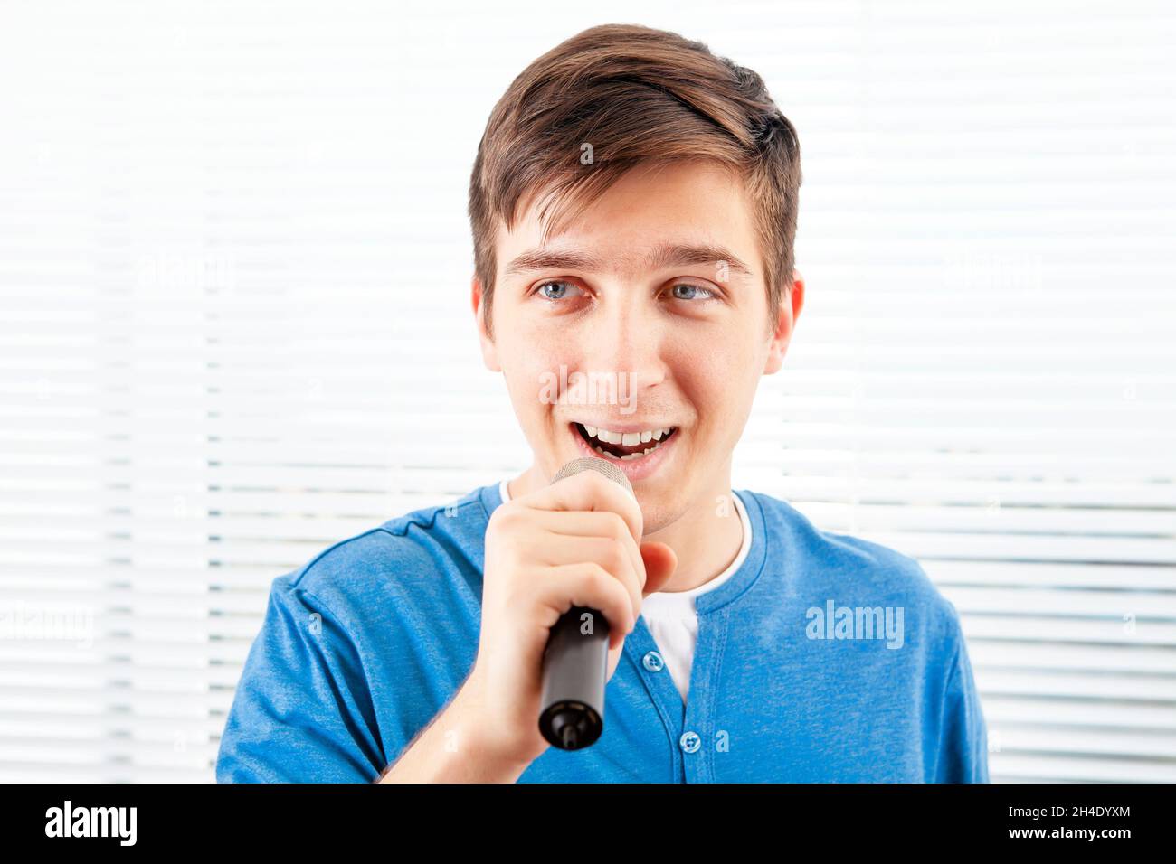 Kerl mit Mikrofon singt ein Lied auf dem Jalousie-Hintergrund Stockfoto