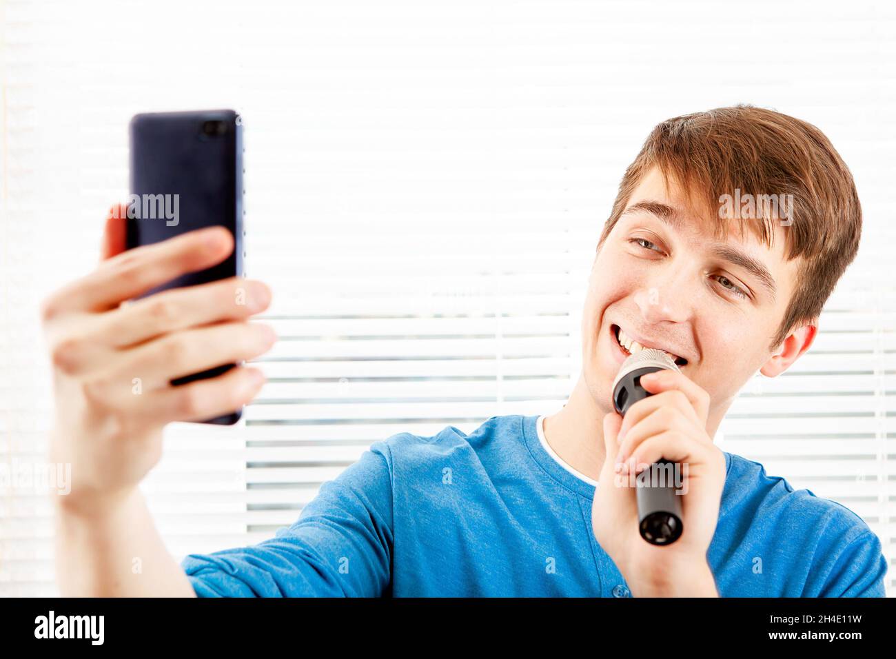 Glücklicher junger Mann mit Mikrofon singt ein Lied und schaut auf das Mobiltelefon Stockfoto