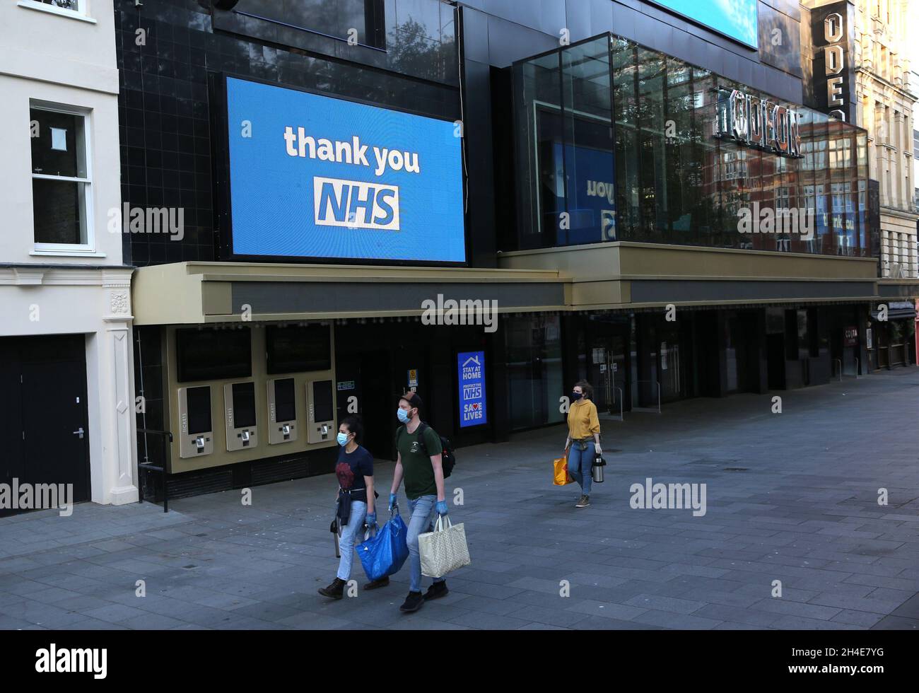 Menschen mit persönlicher Schutzausrüstung (PSA) laufen am geschlossenen ODEON-Kino am Leicester Square im Zentrum von London vorbei, das eine Botschaft der Unterstützung für den NHS zeigt, da Großbritannien weiterhin in der Blockierung ist, um die Ausbreitung des Coronavirus einzudämmen. Bilddatum: Montag, 27. April 2020. Stockfoto