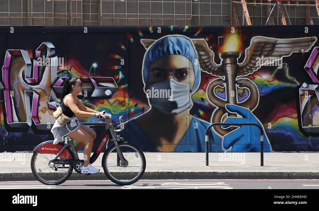 Ein Radfahrer fährt an einem Graffiti vorbei, auf dem ein Gesundheitshelfer mit voller persönlicher Schutzausrüstung in der Nähe von Shoreditch im Osten Londons abgebildet ist, während die Regierung beginnt, einige Sperrmaßnahmen in England zu lockern. Bilddatum: Montag, 1. Juni 2020. Stockfoto