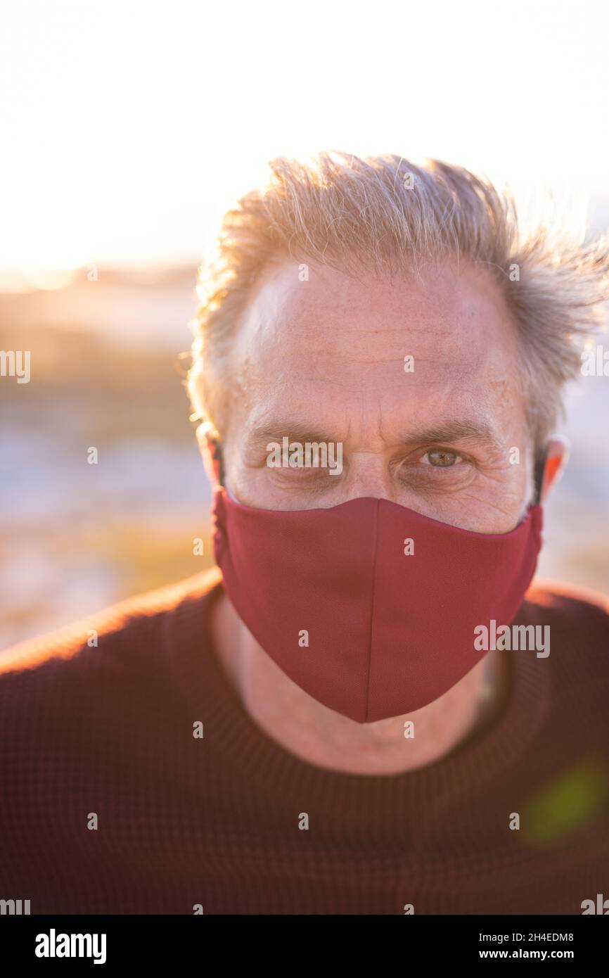 Porträt eines kaukasischen Mannes mit Gesichtsmaske und Blick auf die Kamera am Meer Stockfoto
