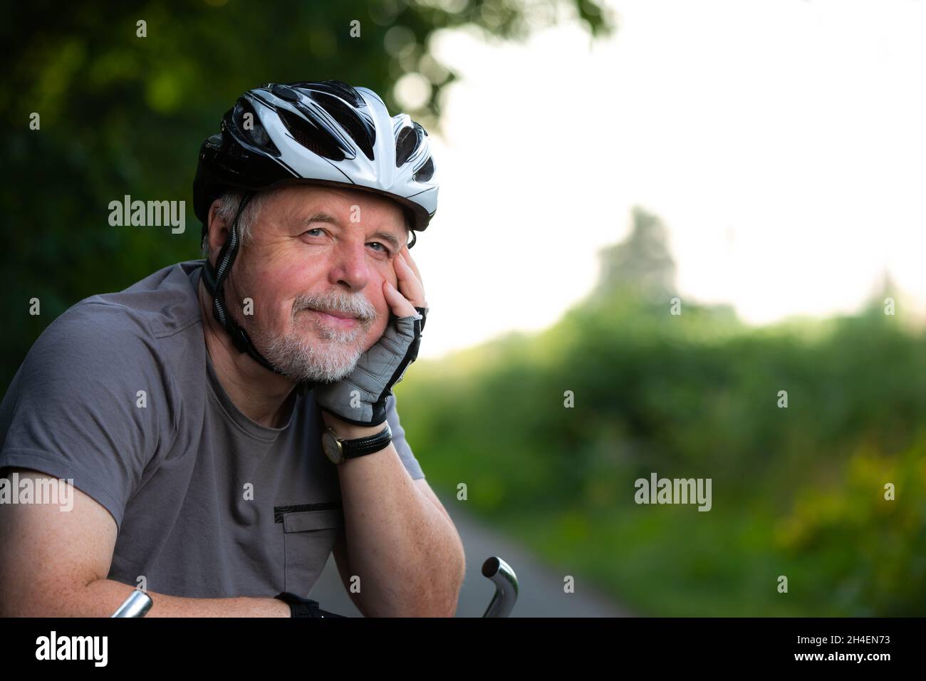 Porträt eines älteren Mannes, der während des schönen Sonnenuntergangs im Sommer Radfahren im Wald genießt, aktiver Rentner Stockfoto