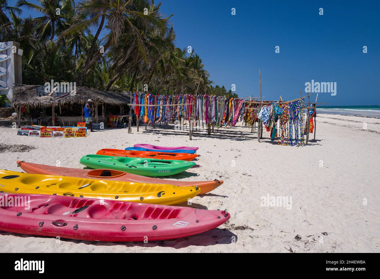 Vor einem Wassersportgeschäft mit tropischem Strand und indischem Ozean im Hintergrund, Diani, Kenia, werden verschiedene Wassersportgeräte ausgestellt Stockfoto