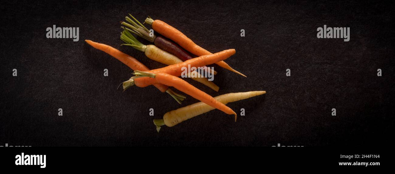 Bunte Erbstück Karotten auf einem dunklen Schiefer Hintergrund Stockfoto