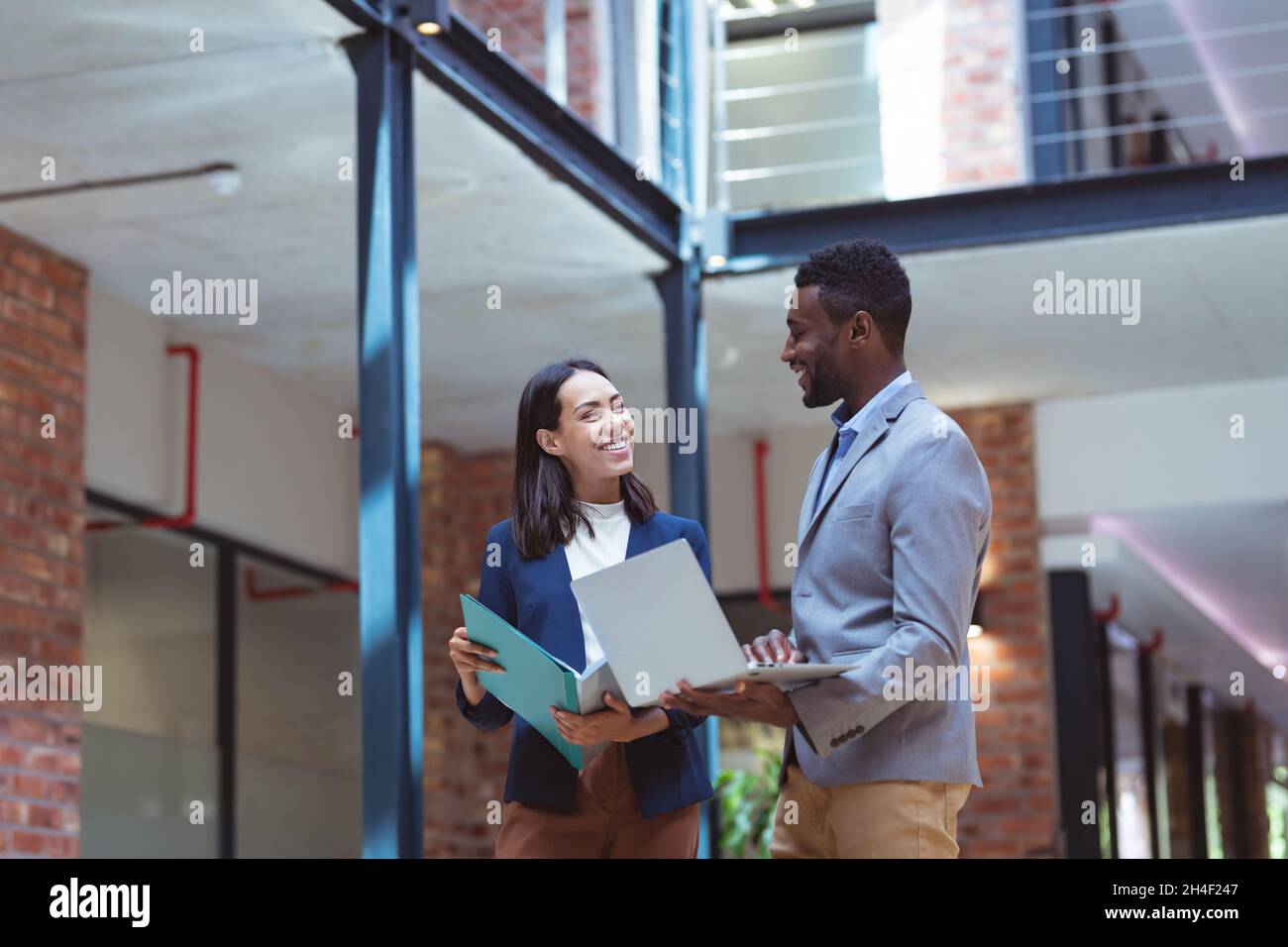 Zwei verschiedene Geschäftsleute, die im modernen Büro lächeln und mit Kollegen im Hintergrund sprechen Stockfoto