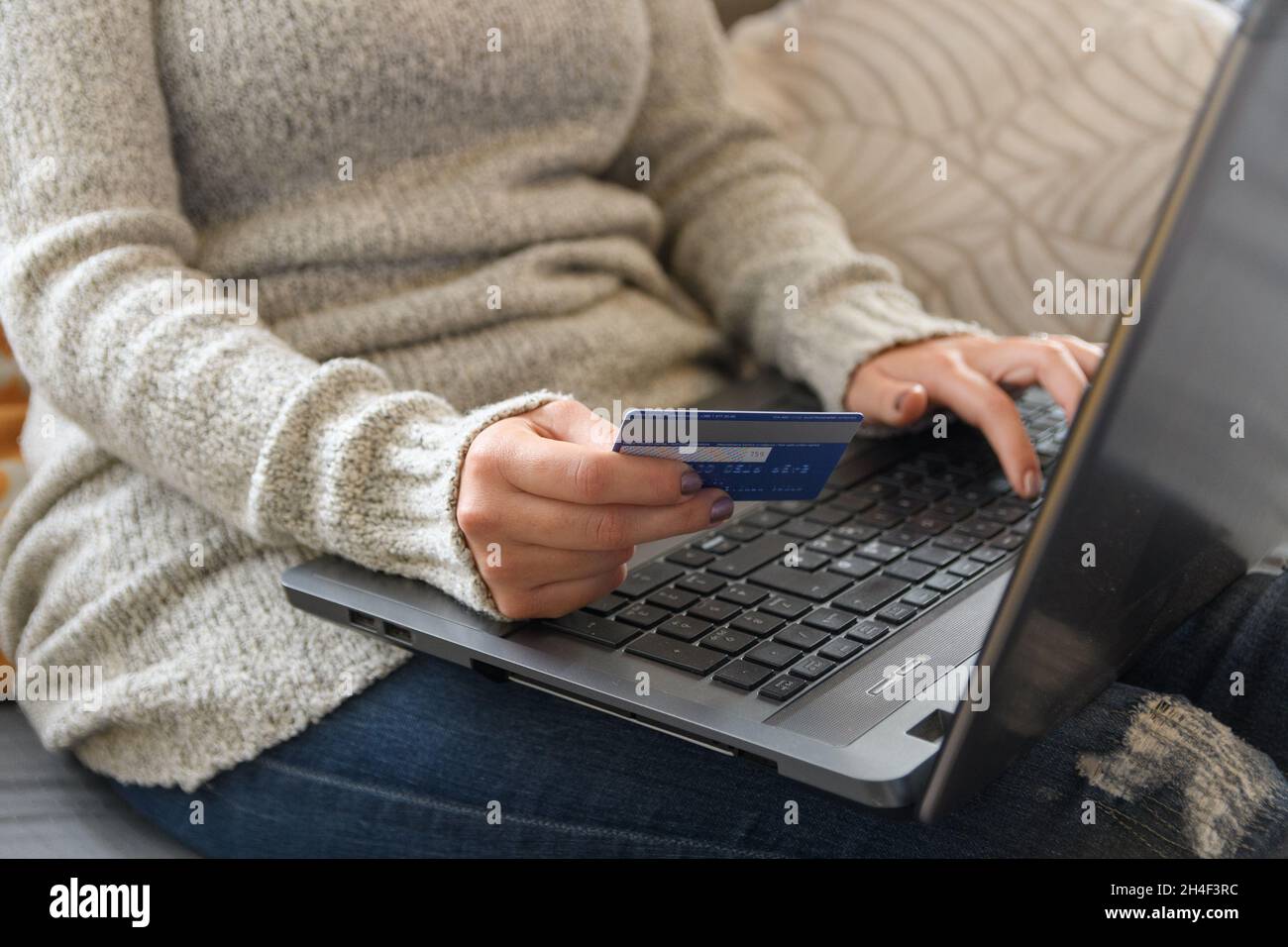 Nahaufnahme Frau in warmen Kleidern sitzt auf der Couch, hält Kreditkarte, während Online-Shopping auf dem Laptop Stockfoto