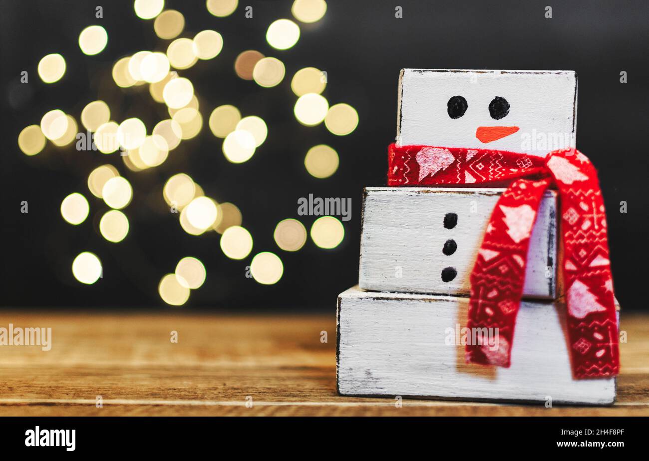 Nahaufnahme eines weißen Schneemanns aus Holz vor dunklem Hintergrund mit Bokeh-Lichtern Stockfoto