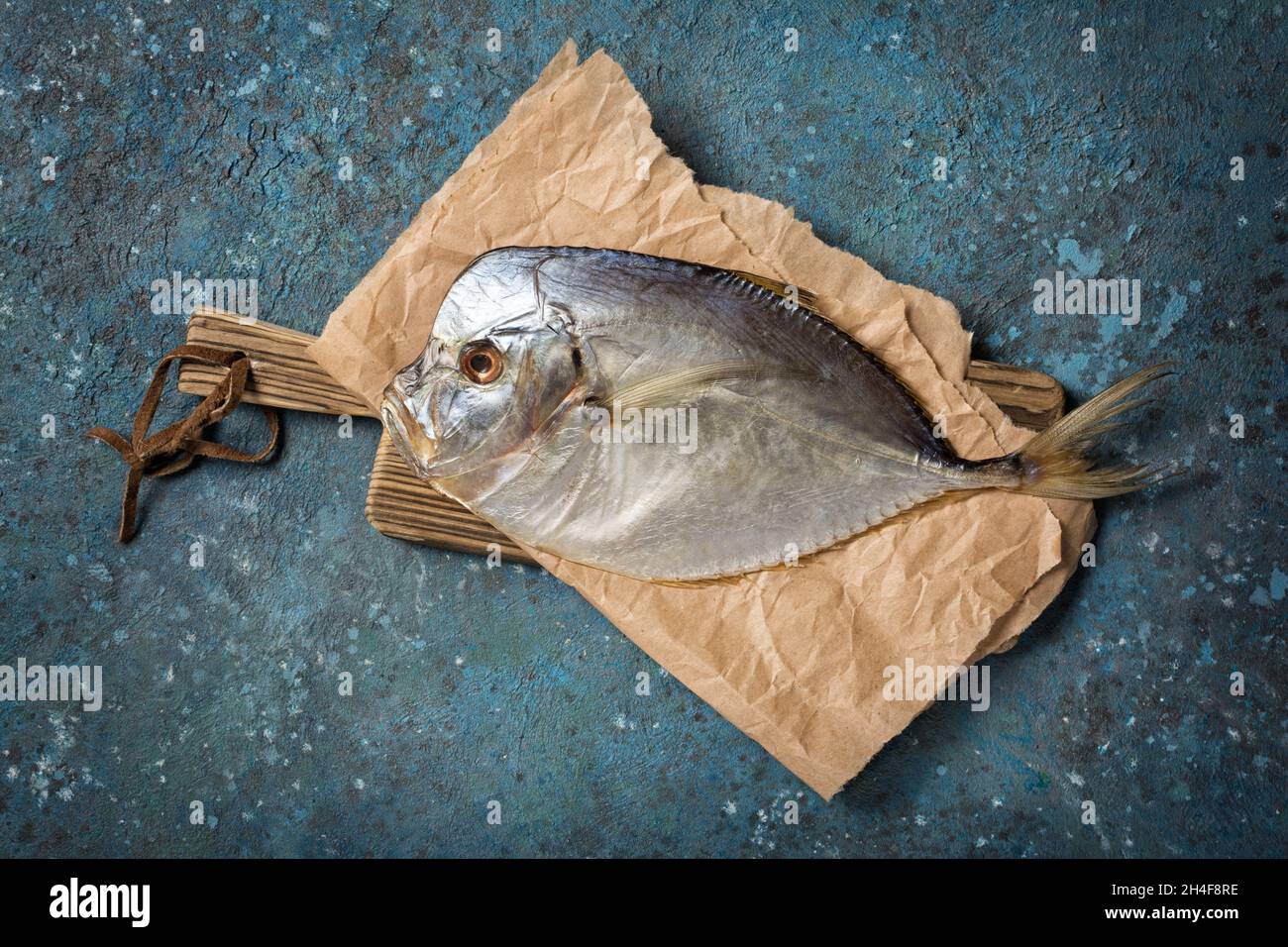 Draufsicht auf leckeren salzigen getrockneten Seefischerbrochenen oder Selena auf Holzschneidebrett und blauem Betonhintergrund Stockfoto