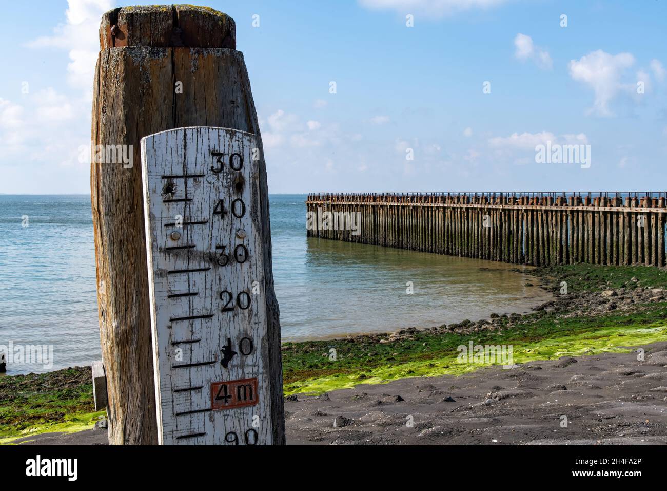 Nahaufnahme einer Wasserstandsanzeige oder Markierung am Strand der Stadt Westkapelle in den Niederlanden mit einem hohen Wellenbrecher im Hintergrund Stockfoto