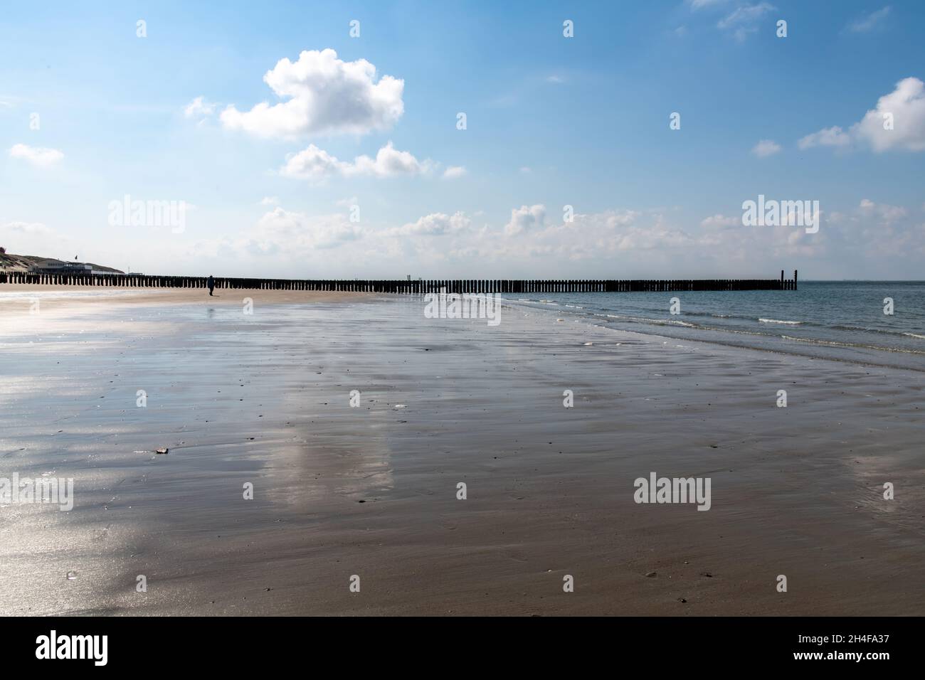Bei Ebbe Blick über den breiten Strand von Westkapelle in den Niederlanden mit typischen hölzernen Wellenbrechern am Sandstrand und Wolken Stockfoto