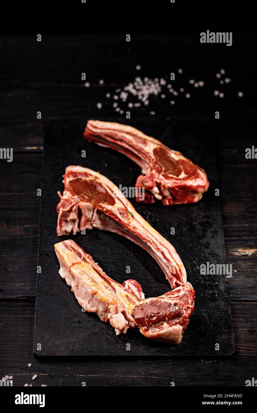 Frische, rohe Lammrippchen. Halal-Fleisch. Rohes Fleisch. Lammkarree auf dunklem rustikalem Hintergrund. Salz und Gewürze. Halal Food Stillleben. Vertikale Aufnahme Stockfoto