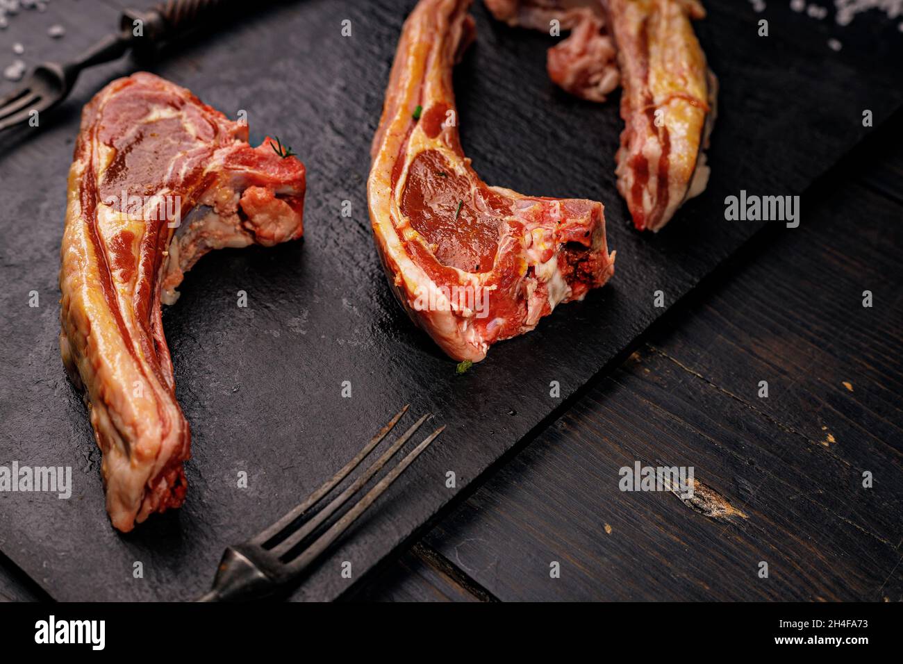 Nahaufnahme von rohen Lammrippen. Halal-Fleisch. Rohes Fleisch. Lammkarree auf dunklem rustikalem Hintergrund. Salz und Gewürze. Halal Food Stillleben. Speicherplatz kopieren Stockfoto