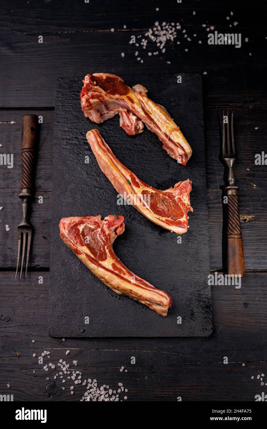Frische, rohe Lammrippchen. Halal-Fleisch. Rohes Fleisch. Lammkarree auf dunklem rustikalem Hintergrund. Salz und Gewürze. Halal Food Stillleben. Vertikale Aufnahme. Speicherplatz kopieren Stockfoto