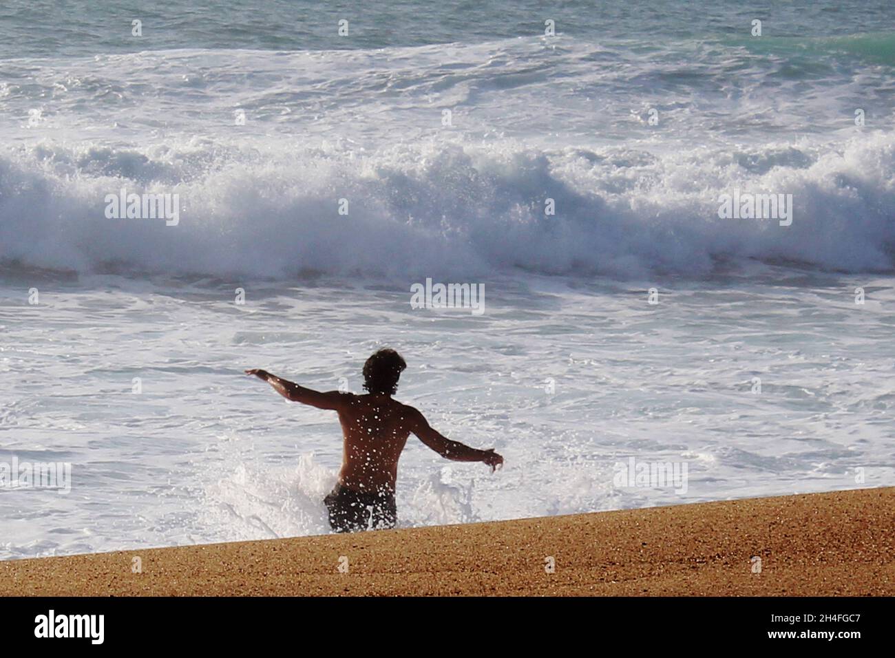 Sportlicher, atraktiver Mann (keine Erkennbarkeit), der in die Wellen läuft, Nazare, Portugal Stockfoto