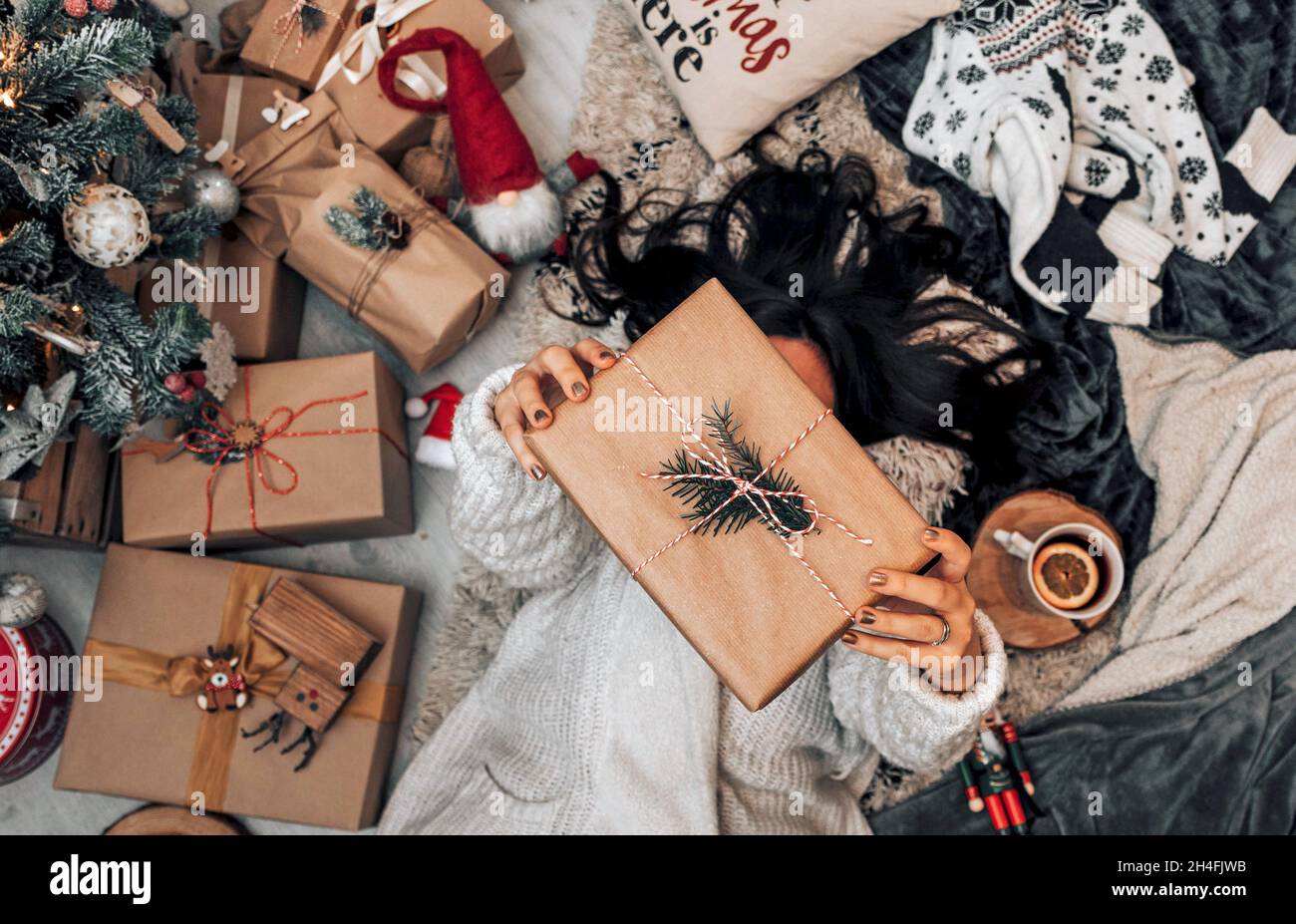 Draufsicht auf die Frau, die am weihnachtsbaum lag und ein eingewickeltes weihnachtsgeschenk hielt. Stockfoto