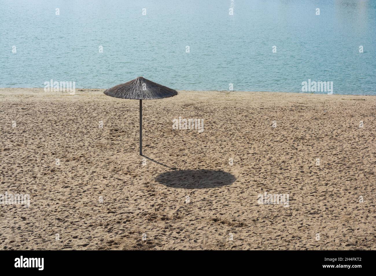 Ein Schilfschirm an einem leeren Strand am Mittag in der Herbstsonne, der einen großen Schatten wirft. Einsamkeit. Stockfoto