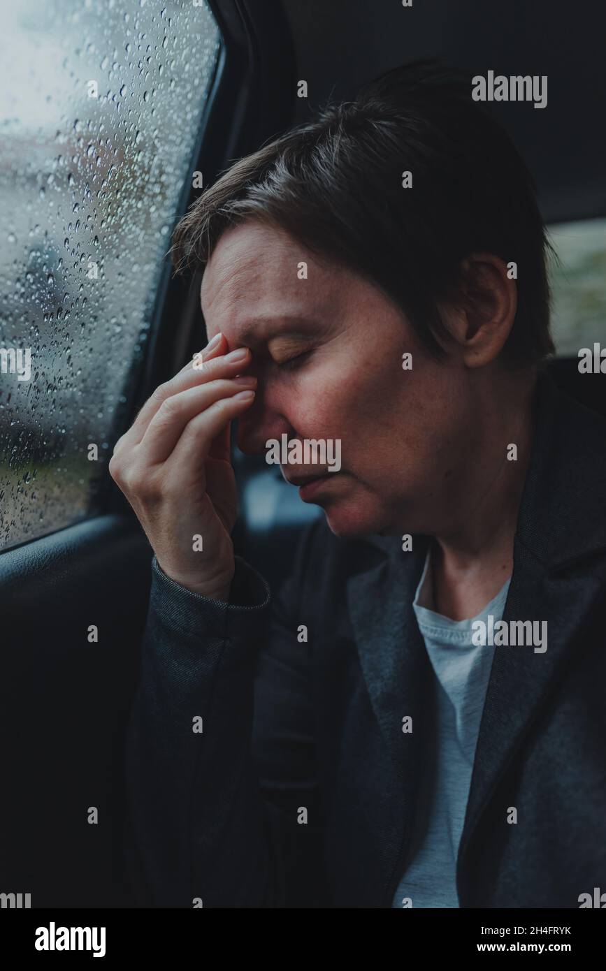 Geschäftsfrau mit starken Kopfschmerzen, die bei Regen auf dem Rücksitz eines Autos sitzt, selektiver Fokus Stockfoto