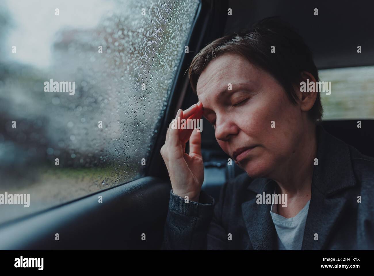 Geschäftsfrau mit starken Kopfschmerzen, die bei Regen auf dem Rücksitz eines Autos sitzt, selektiver Fokus Stockfoto