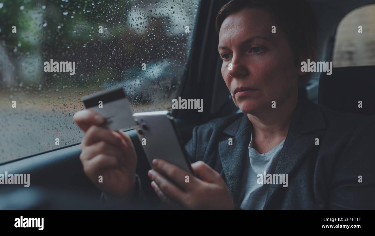 Geschäftsfrau mit Kreditkarte und Handy für E-Banking vom Rücksitz des Autos im Regen, selektive Fokussierung Stockfoto
