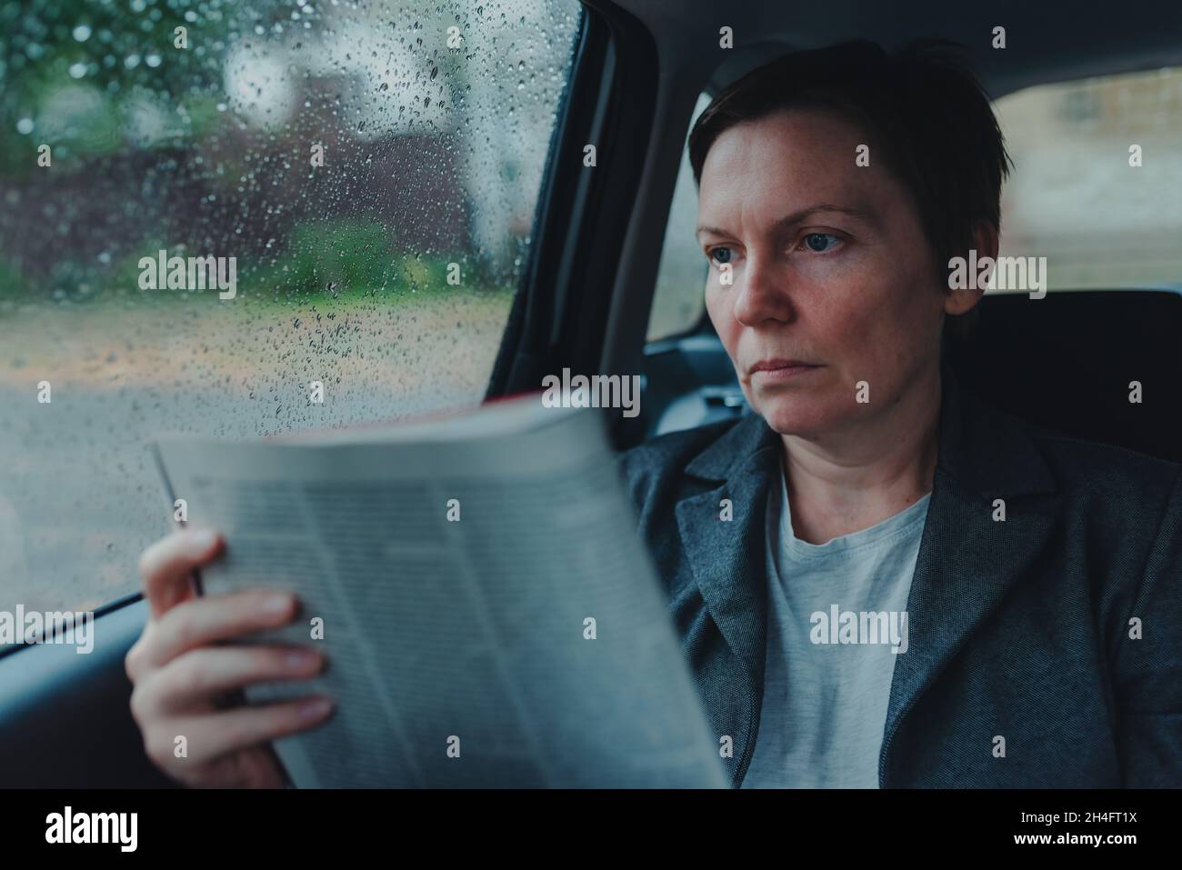 Geschäftsfrau liest Geschäftsbericht auf dem Rücksitz eines Autos während des Regens, selektiver Fokus Stockfoto