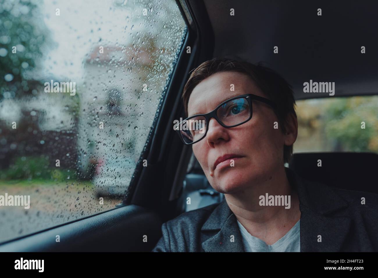 Besorgte Geschäftsfrau mit Brillen, die im Auto warten und bei Regen aus dem Fenster schauen, selektiver Fokus Stockfoto