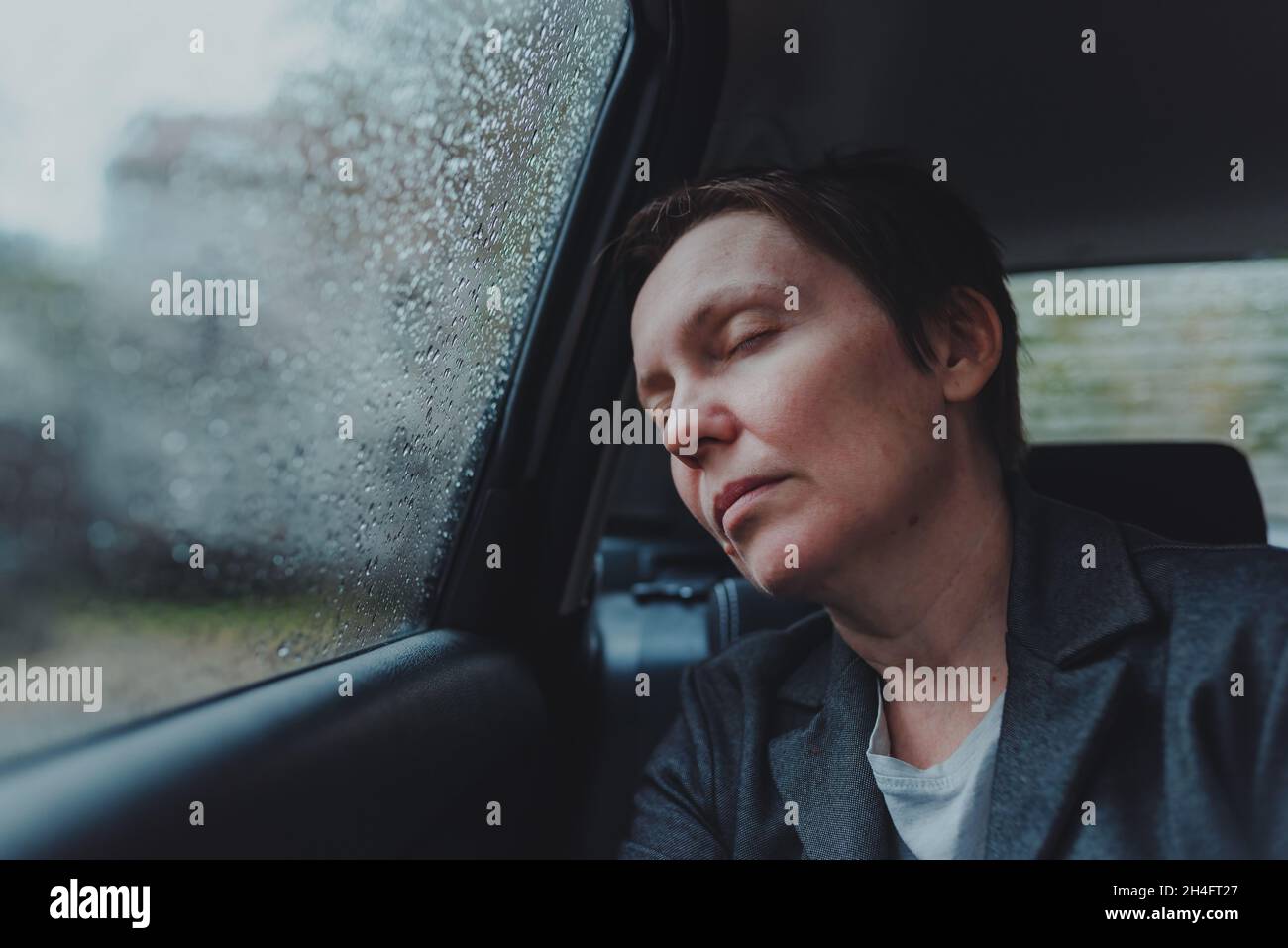 Müde erschöpfte Geschäftsfrau, die bei Regen auf dem Rücksitz des Autos schläft, selektiver Fokus Stockfoto