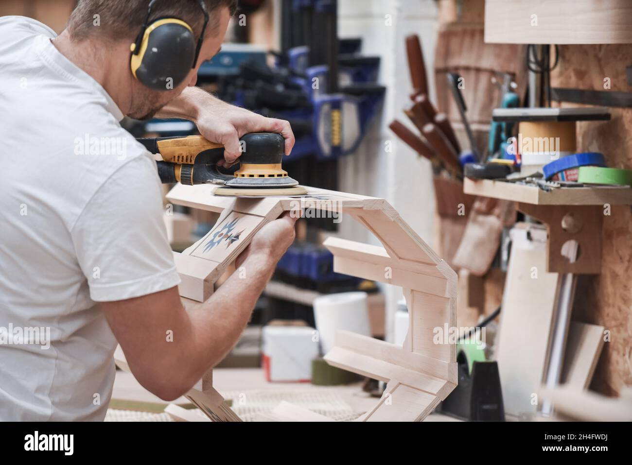Ein Mann, der mit einem Elektroschleifer für Elektrowerkzeuge Holz in der Tischlerei basteln kann Stockfoto
