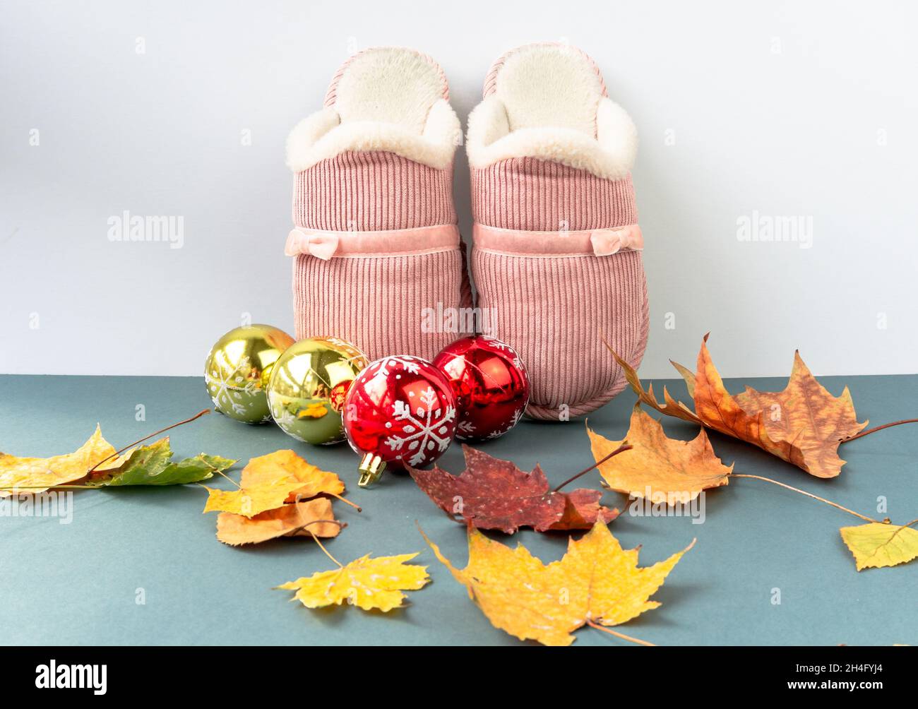 Warme und komfortable Hausschuhe mit gelben Blättern und Weihnachtsdekoration auf grünem Hintergrund. Rosa Farbe. Stockfoto
