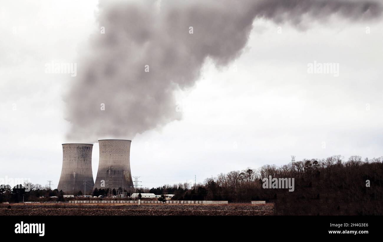 Fernansicht von zwei industriellen Rauchgasen, die Treibhausgase in die Atmosphäre spucken, und daneben ein Wald- und Strommasten. Wahrscheinliche CO Stockfoto