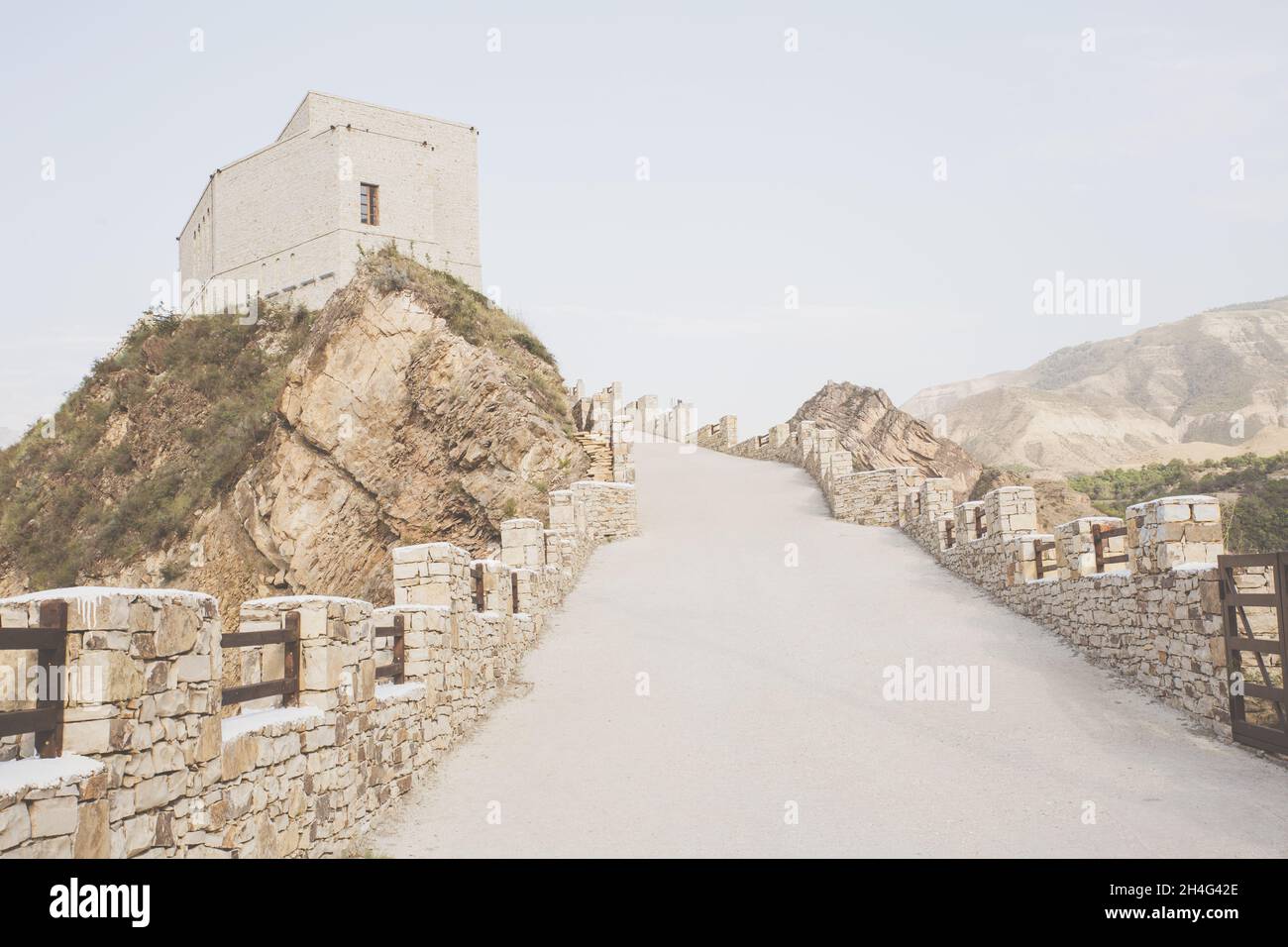 Eine Straße mit einem Steinzaun, die zum alten Turm auf der Spitze des Berges, Sepia, führt. Historische Orte. Ganz nach oben. Reisen, Wandern. Berge Akhulgo Stockfoto