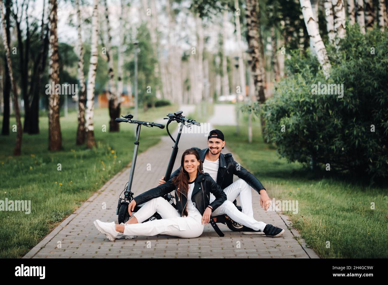 Porträt eines Paares, das in der Nähe von Elektrorollern sitzt, gemeinsam Zeit in der Natur genießt, zwei Liebhaber auf Elektrorollern.Menschen auf Rollern. Stockfoto
