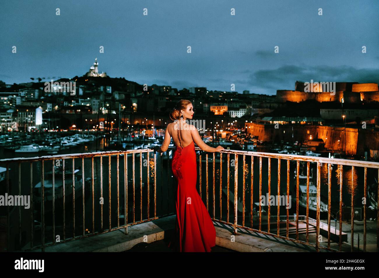 Ein elegantes Mädchen in einem roten Abendkleid auf den Straßen der Nachtstadt Marseille.Eine Frau in einem roten Abendkleid in Frankreich. Stockfoto