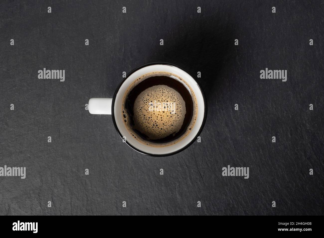 Eine Tasse Kaffee mit schönem Schaum in der Nähe Kaffeebohnen sind auf einem schwarzen Stein Hintergrund Draufsicht Kopierfläche verstreut Stockfoto