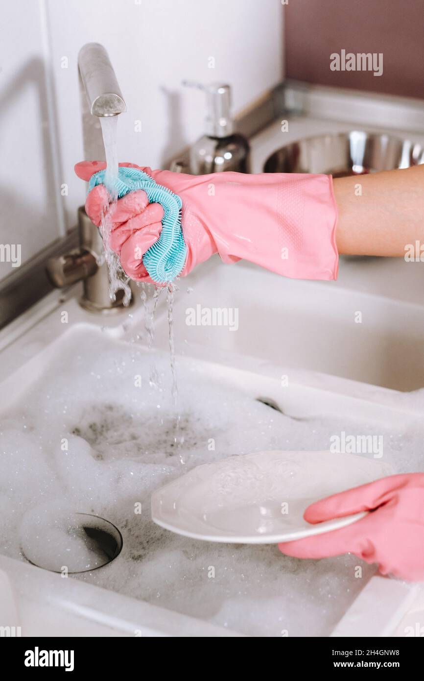 Hausfrau Mädchen in rosa Handschuhe wäscht Geschirr von Hand in der Spüle mit Waschmittel. Das Mädchen putzt das Haus und wäscht Geschirr mit Handschuhen zu Hause Stockfoto