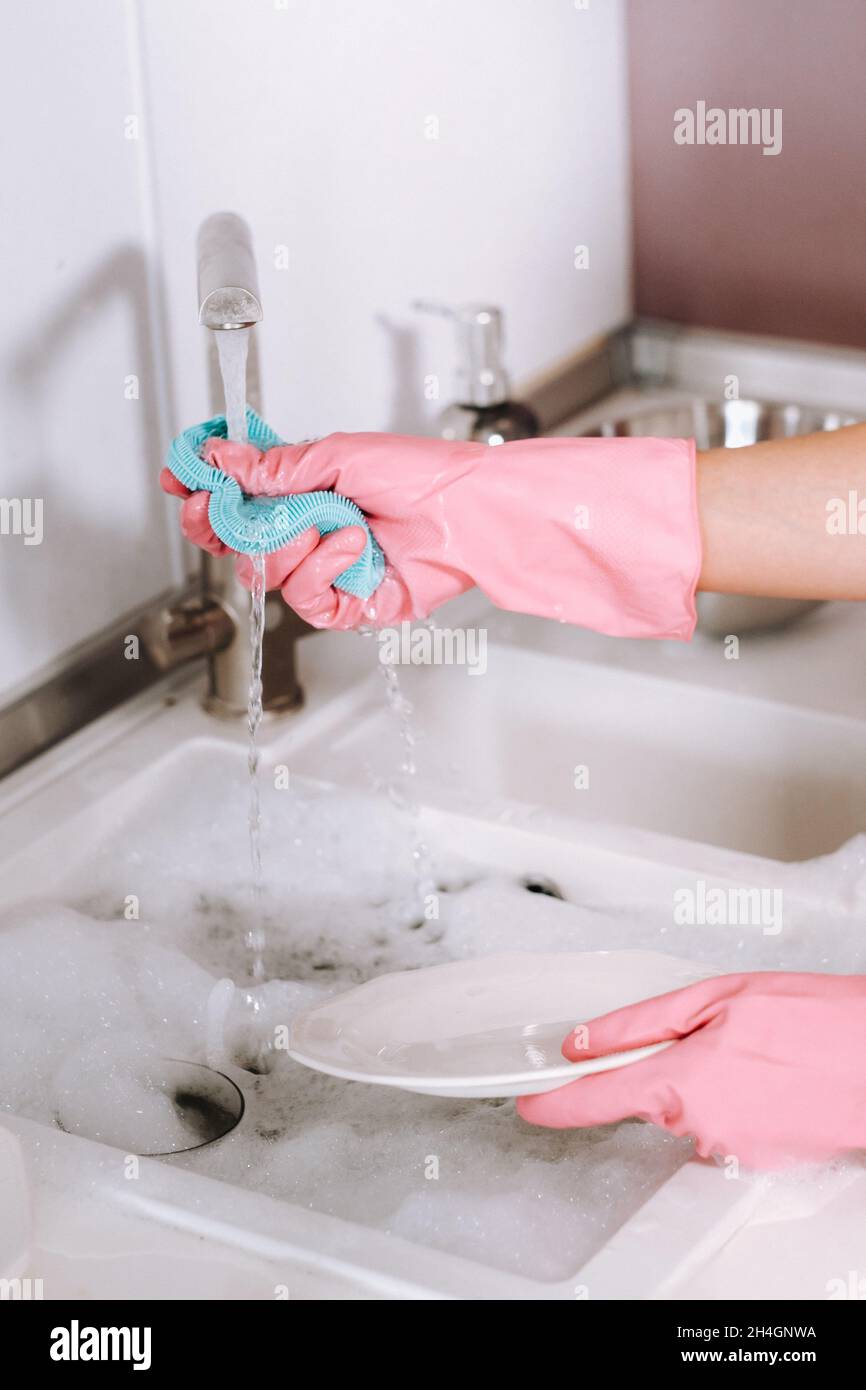 Hausfrau Mädchen in rosa Handschuhe wäscht Geschirr von Hand in der Spüle mit Waschmittel. Das Mädchen putzt das Haus und wäscht Geschirr mit Handschuhen zu Hause Stockfoto