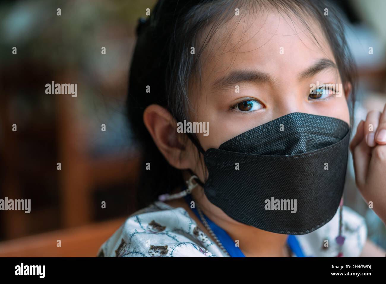 Nahaufnahme Gesicht der asiatischen Kind Mädchen trägt medizinische schwarze Farbmarke, emotionale Augen Blick auf die Kamera, verschwommene Hintergrund Menschen im Restaurant. Stockfoto