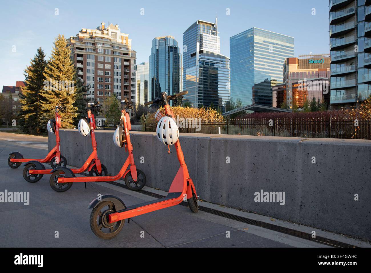 Reihe von gemeinsam genutzten E-Scootern zur Miete in der Innenstadt, mit dem weltweit ersten App-gesteuerten Helmschloss, das bei jeder Vermietung einen Schutzhelm bietet. Stockfoto