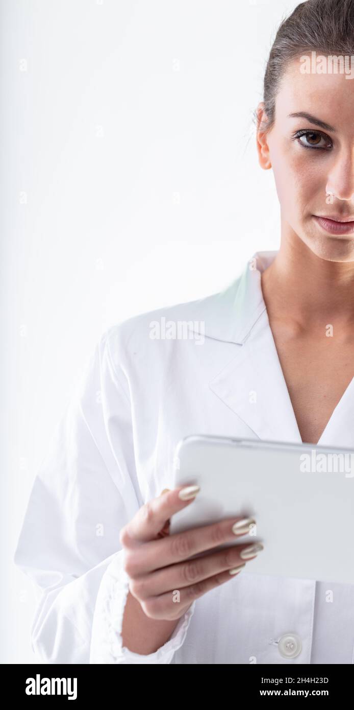 Ein halbportrait mit einer Ärztin oder Krankenschwester im weißen Laborkittel, die einen Tablet-pc hält und die Kamera mit ernstem Gesichtsausdruck anschaut Stockfoto